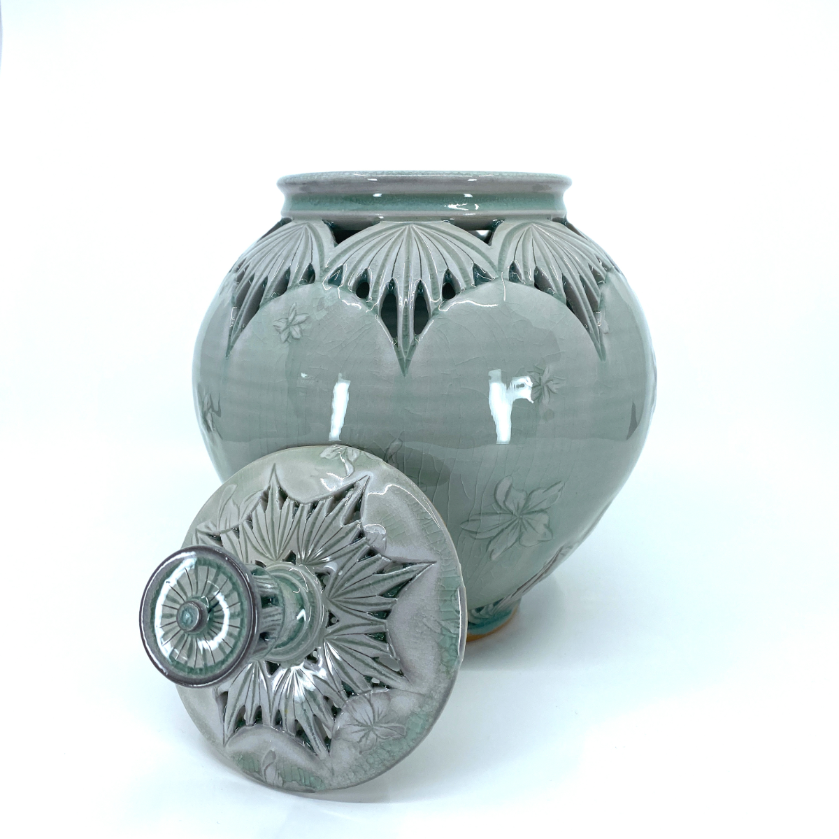 Celadon lidded jar with pierced petal carving, lid resting in front