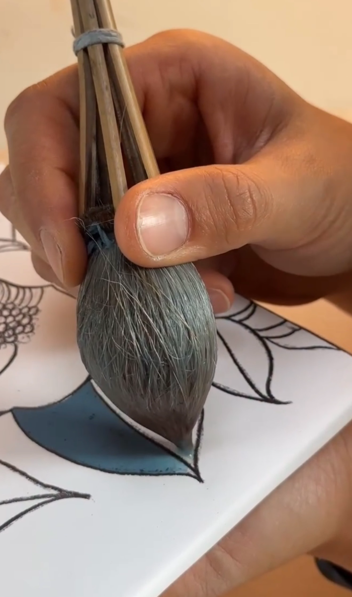 A loaded brush laying blue-grey overglaze inside a black-outlined petal