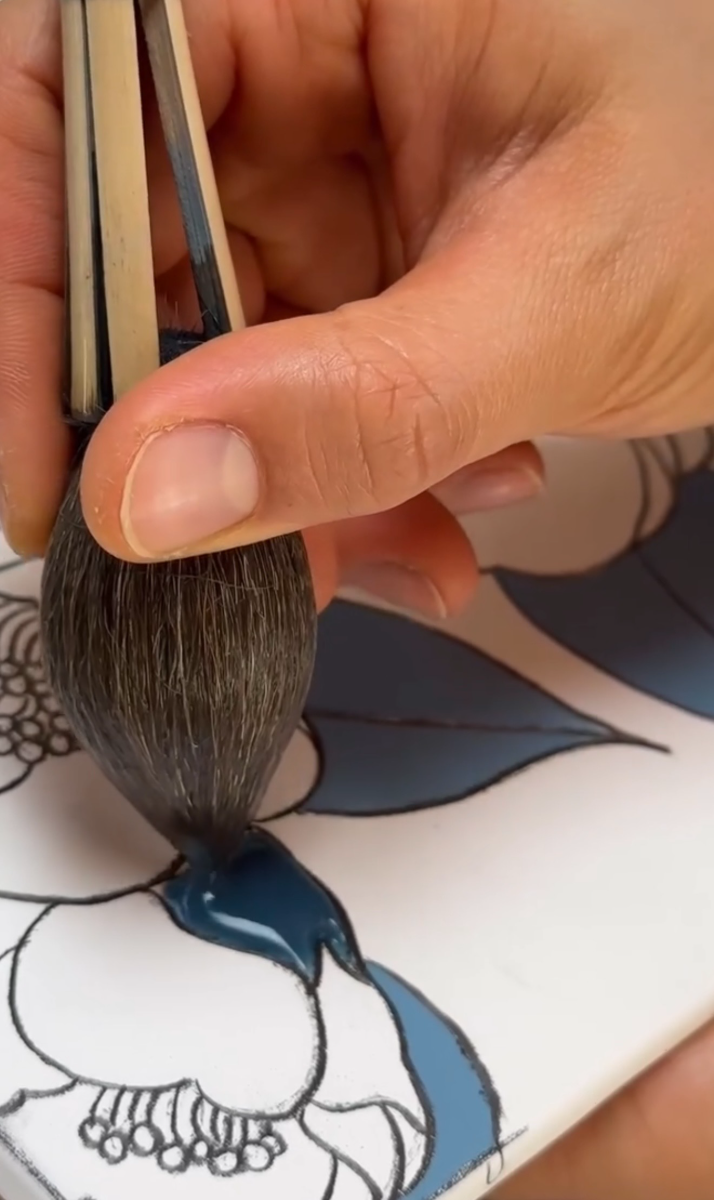 Deep blue overglaze being brushed into a petal outline on a tile