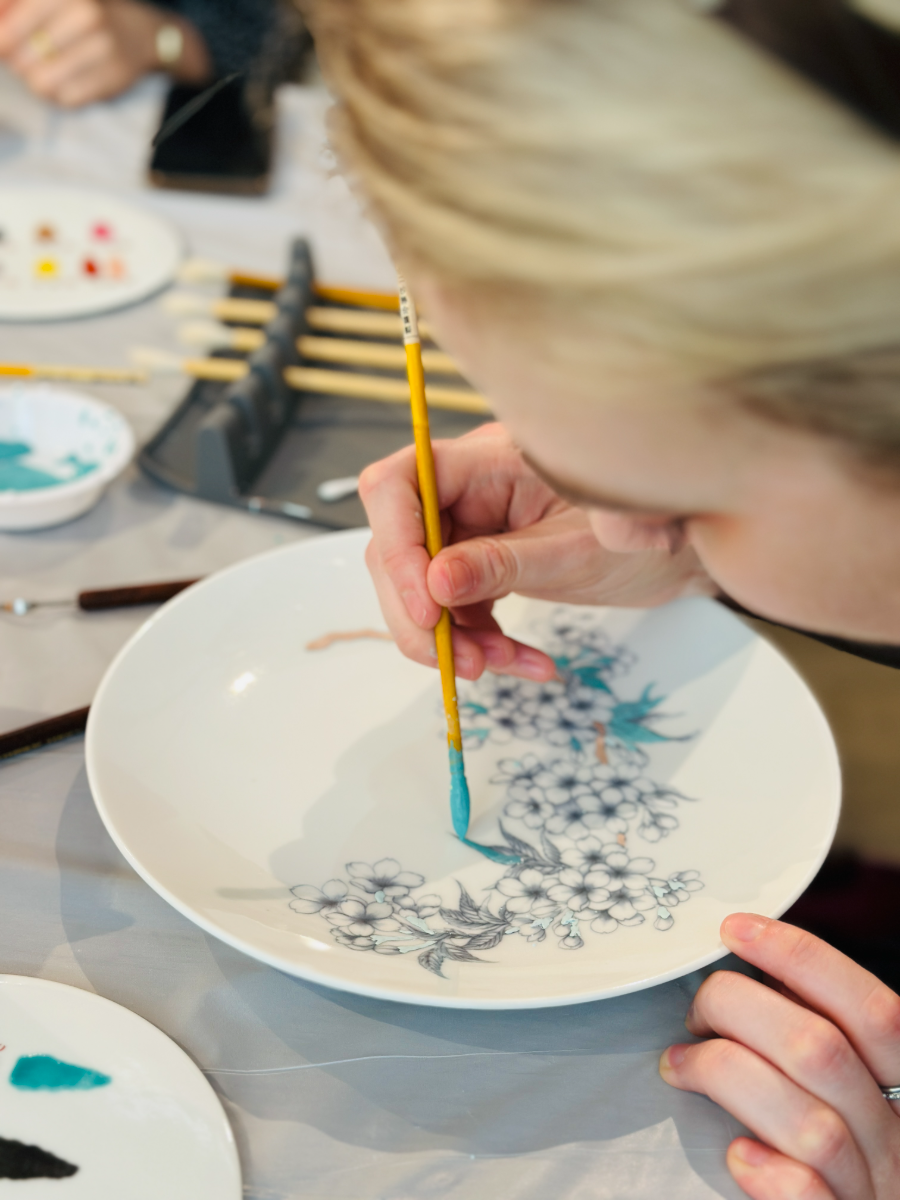 A student laying teal overglaze into an outlined cherry-blossom design