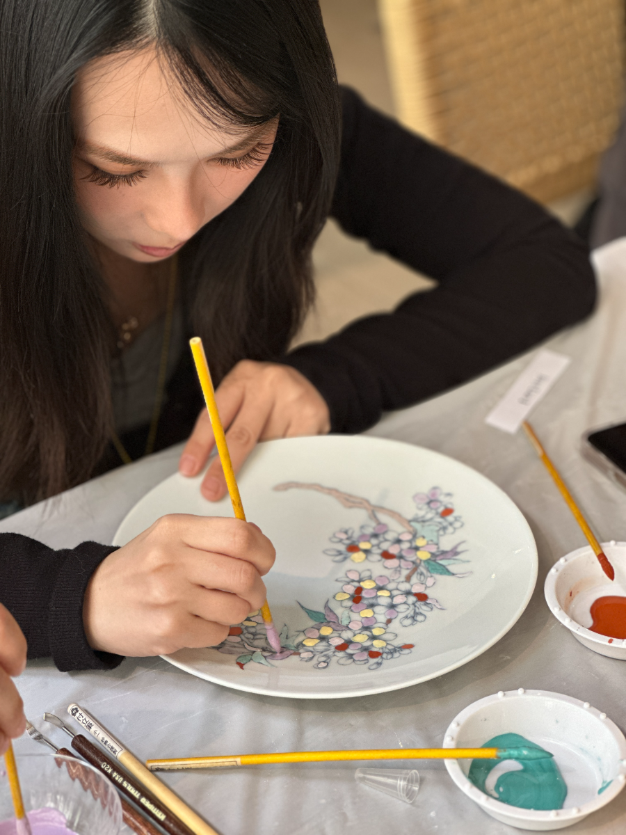 A student painting lilac and yellow blossoms onto a plate